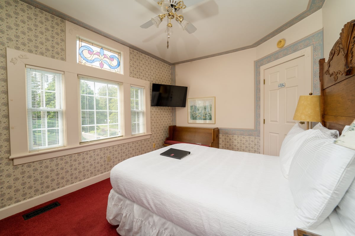 A neatly arranged bedroom with a bed, a television, and a window with blinds.