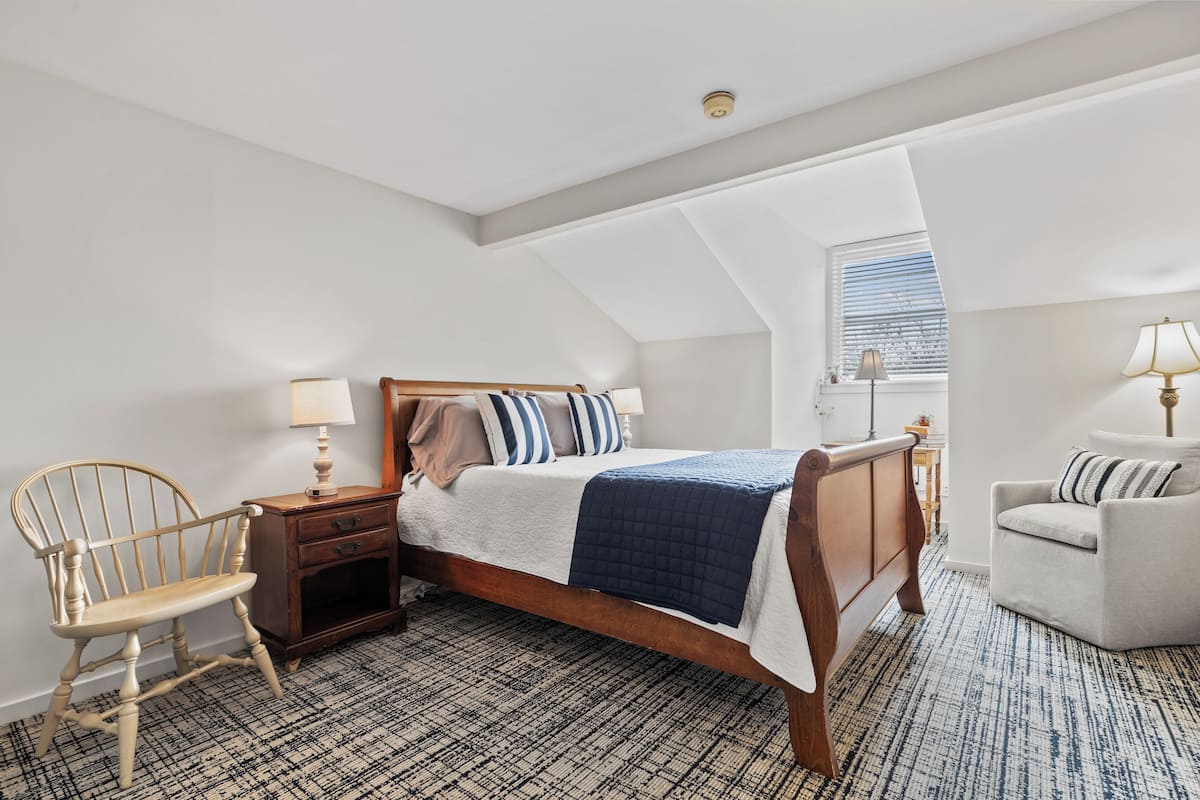 A bedroom with a wooden bed, a chair, a nightstand, and a lamp.