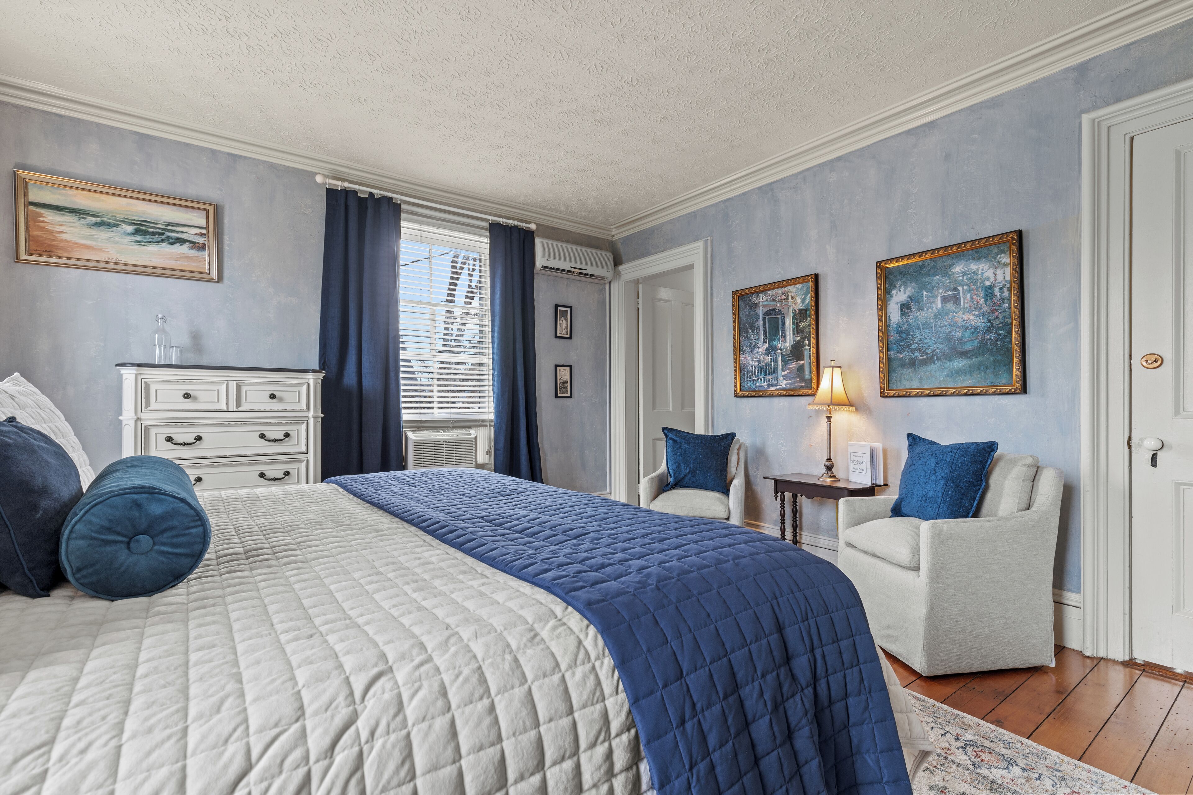 Une chambre à coucher avec un grand lit, une commode, une chaise et deux tableaux accrochés au mur.