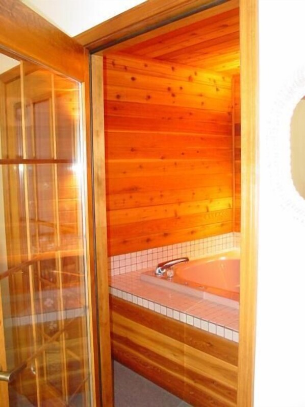 A wooden sauna room with a glass door, a tiled floor, and a bathtub. - Woodland Motor Lodge (Grayling)