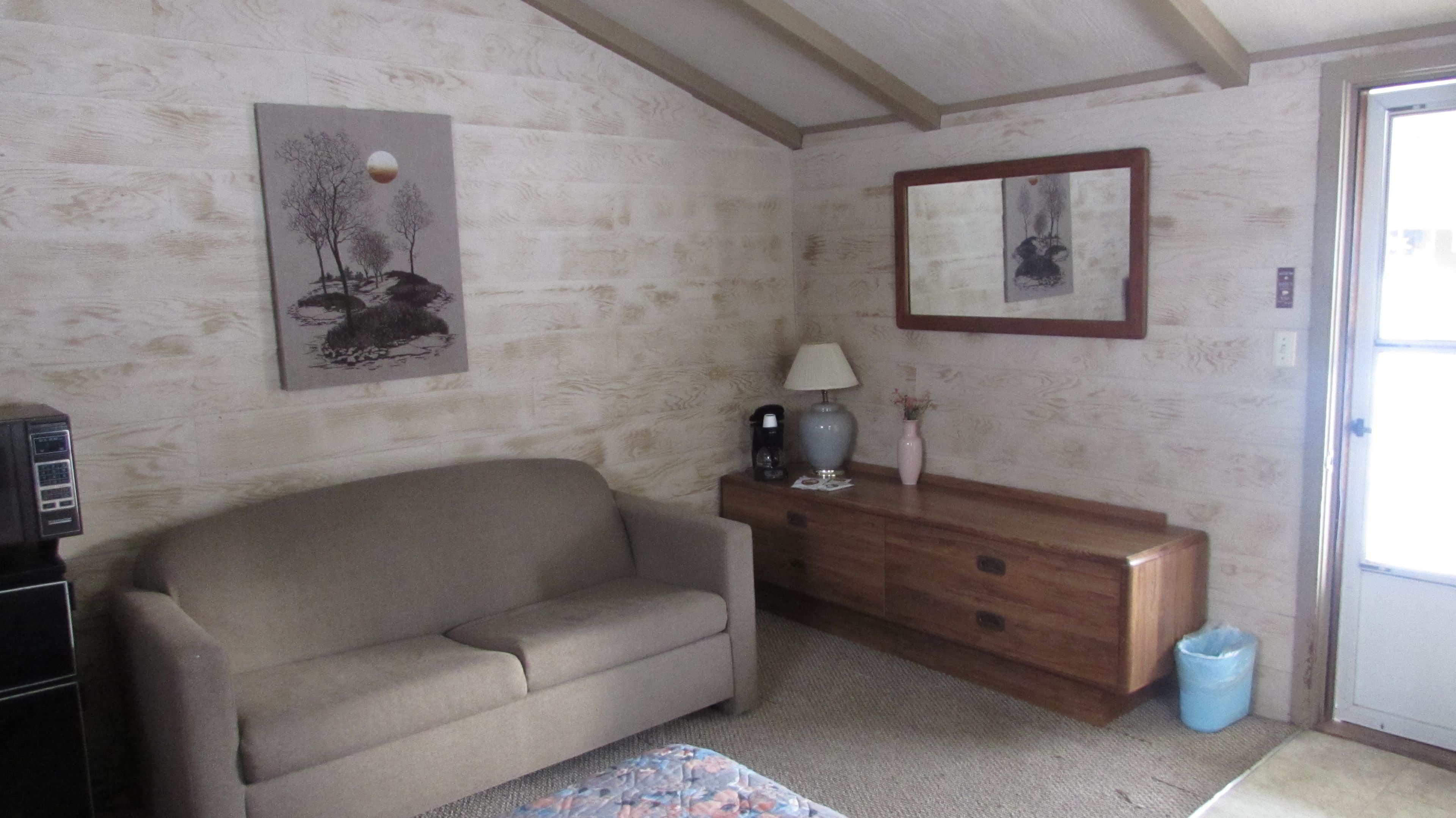 Una sala de estar con un sofá, un aparador de madera, una lámpara y un cuadro en la pared.