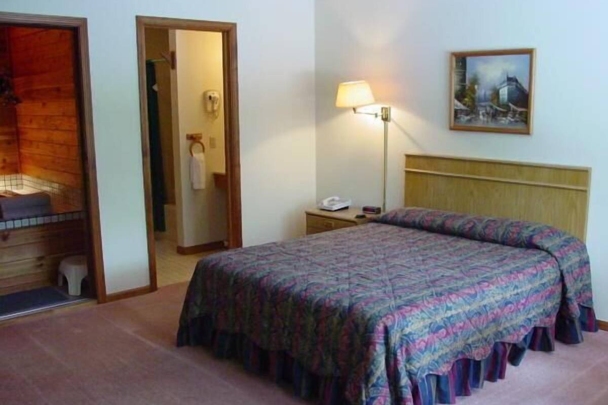A hotel room with a bed, a nightstand, a lamp, and a painting on the wall.
