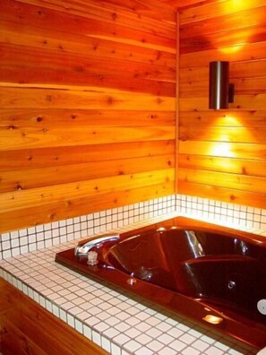A wooden cabin interior with a tiled floor, a wooden ceiling, and a black bathtub. - Woodland Motor Lodge (Grayling)