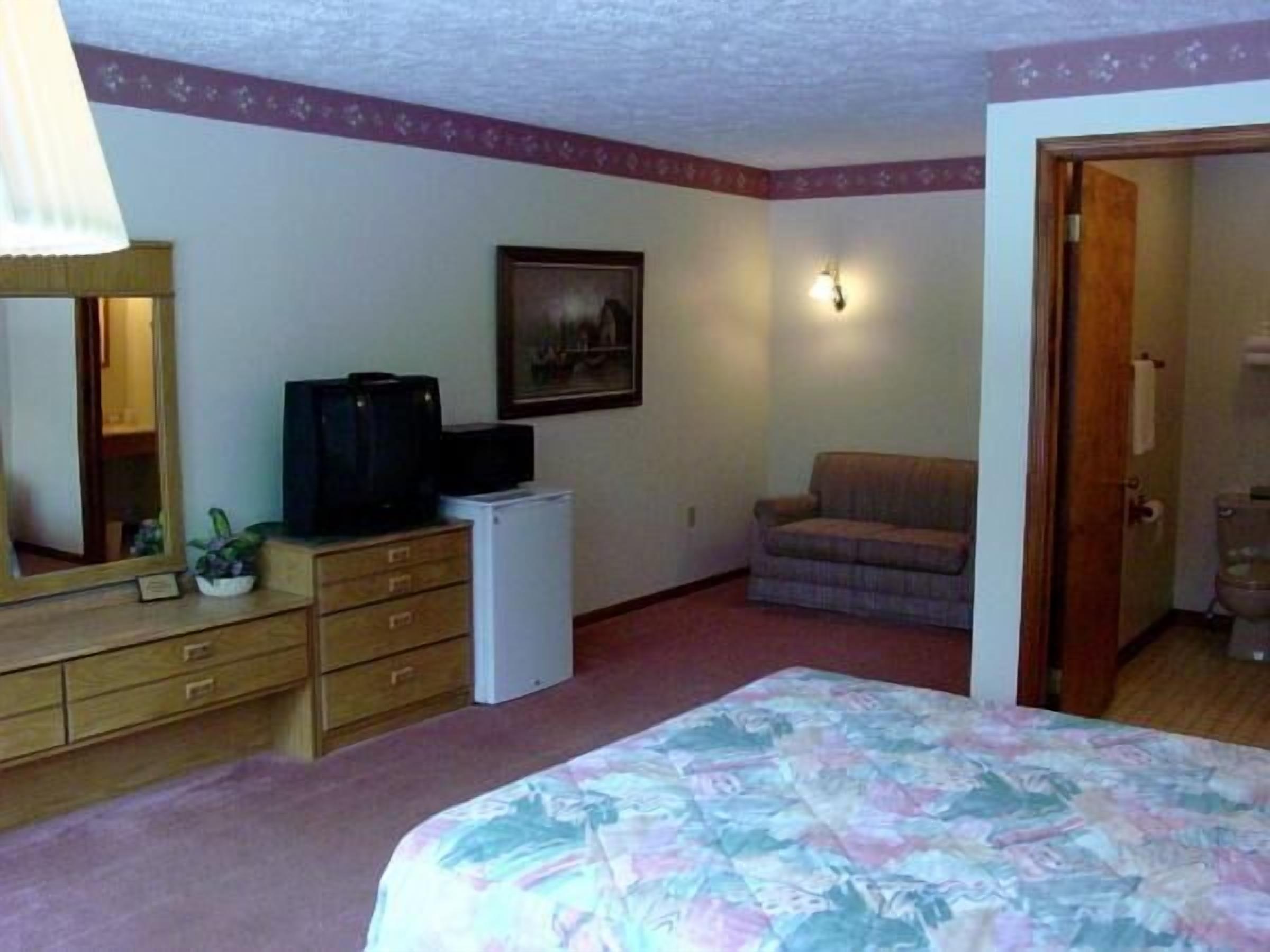 A bedroom with a bed, dresser, television, and a painting on the wall.