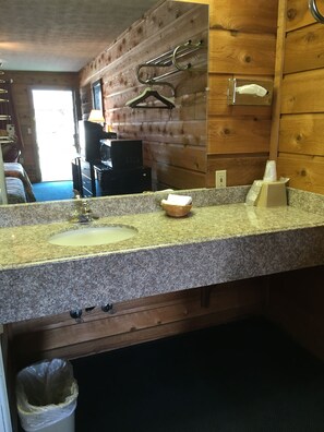 Une salle de bain avec un comptoir en granit, un lavabo, un miroir, un distributeur de serviettes et des panneaux de bois au mur.