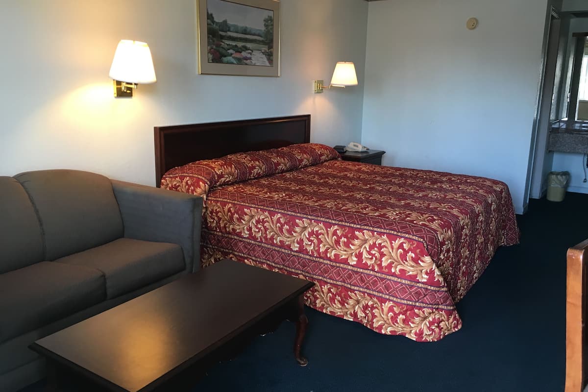 A hotel room with a bed, a sofa, a small table, two wall lamps, and a painting on the wall.