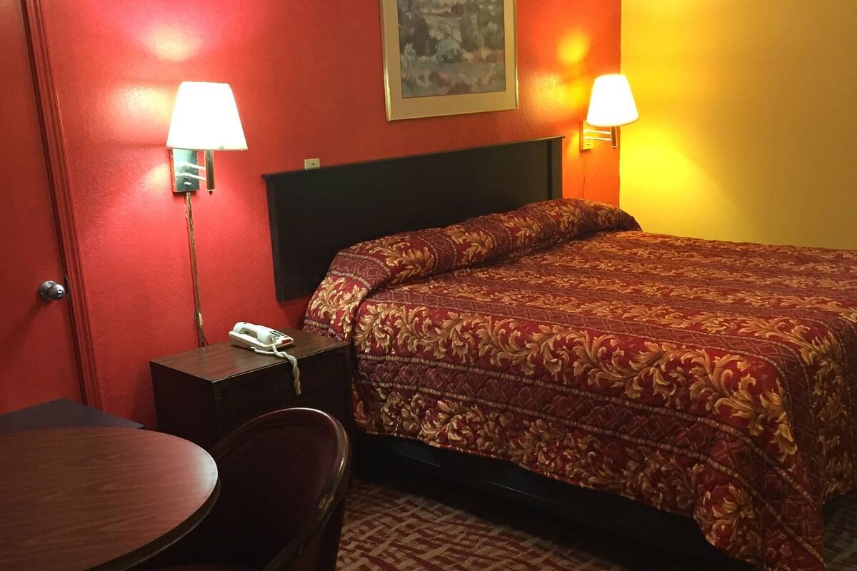 A hotel room with a bed, two bedside lamps, a desk with a telephone, and a chair.