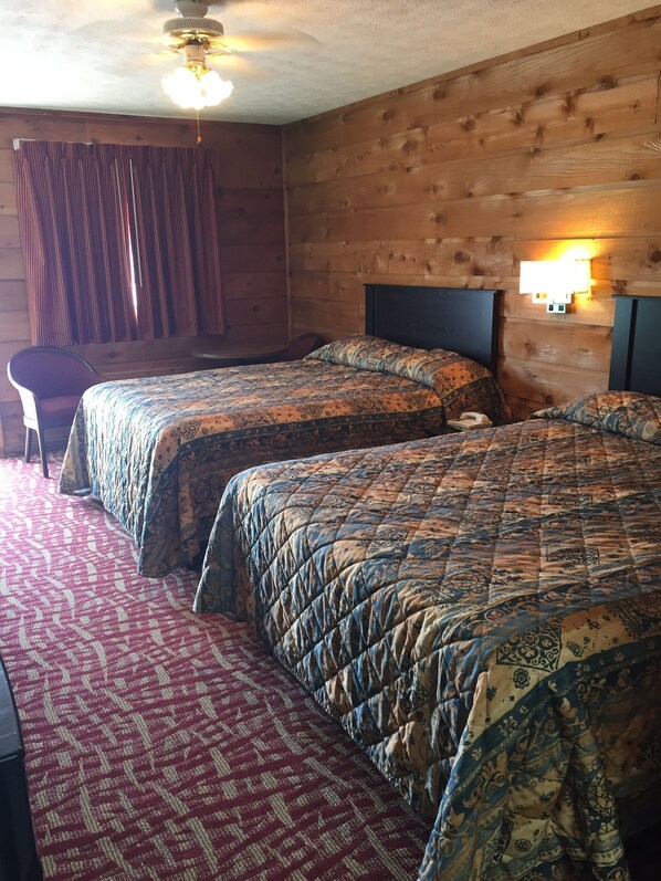A room with two beds, a chair, a ceiling fan, and a wall-mounted light fixture.