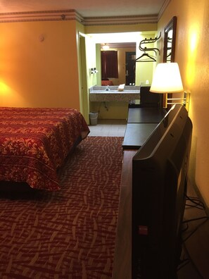 A hotel room with a bed, a desk, a television, and a bathroom visible in the background.
