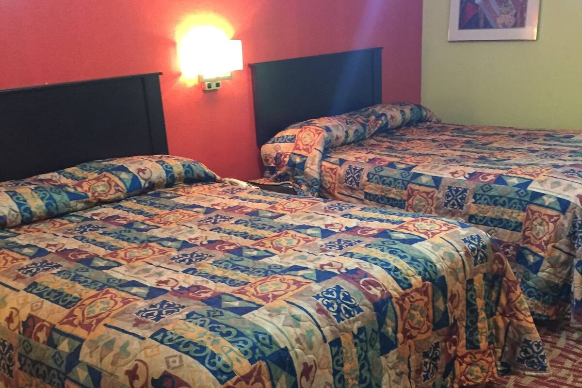 A hotel room with two beds, each with a patterned bedspread, a headboard, and a wall-mounted light.