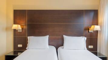 Habitación de hotel con dos camas, cabecera de madera oscura, lámparas de noche y mesitas de noche con lámparas.
