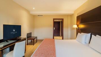 Una habitación de hotel con una cama, un escritorio con televisor, una silla y una mesita de noche.
