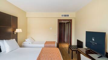 Quarto de hotel com duas camas, uma escrivaninha com televisão e uma porta que dá para um corredor.
