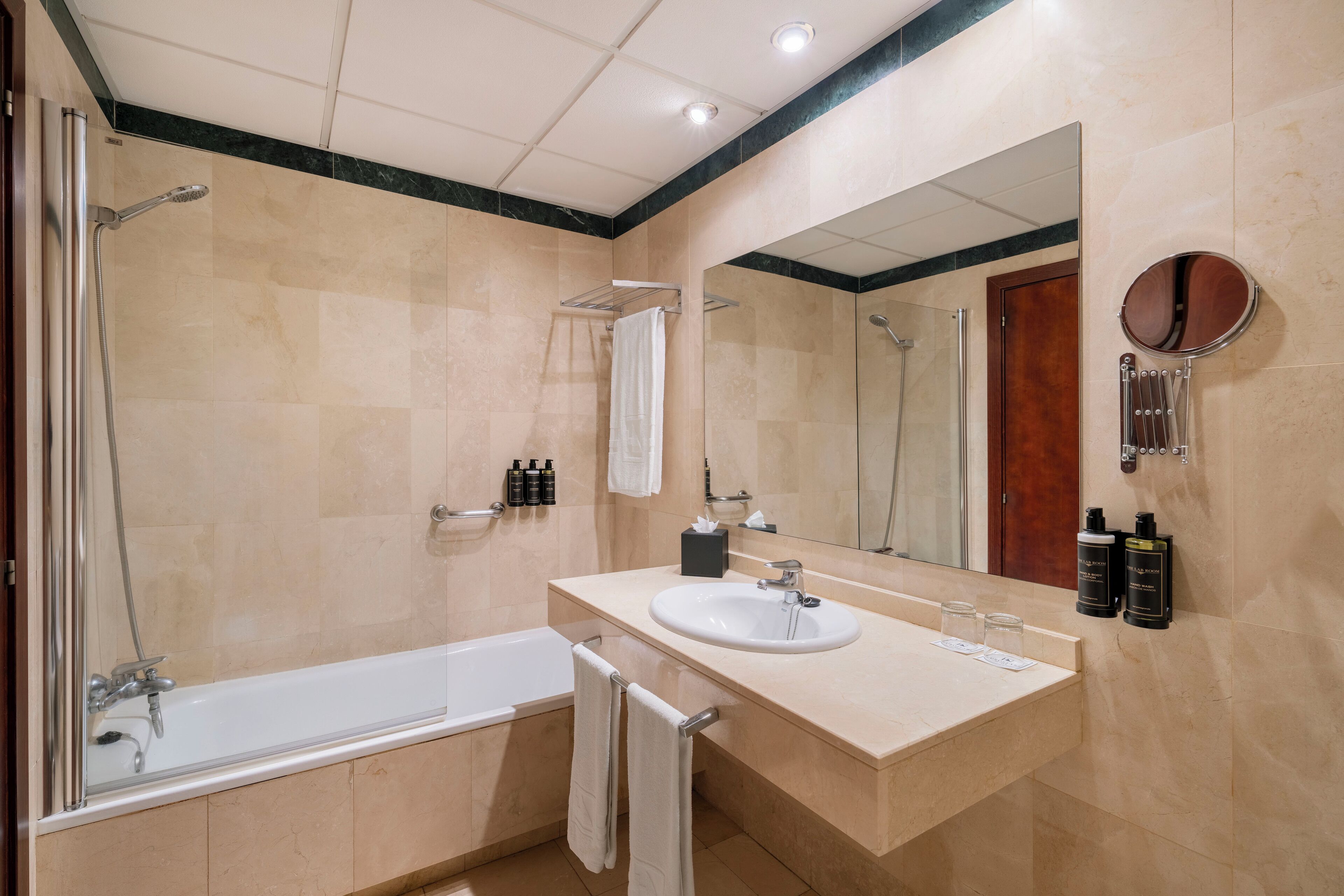Un baño moderno con bañera, lavamanos y ducha. Hay artículos de aseo en la pared y un perchero para toallas.