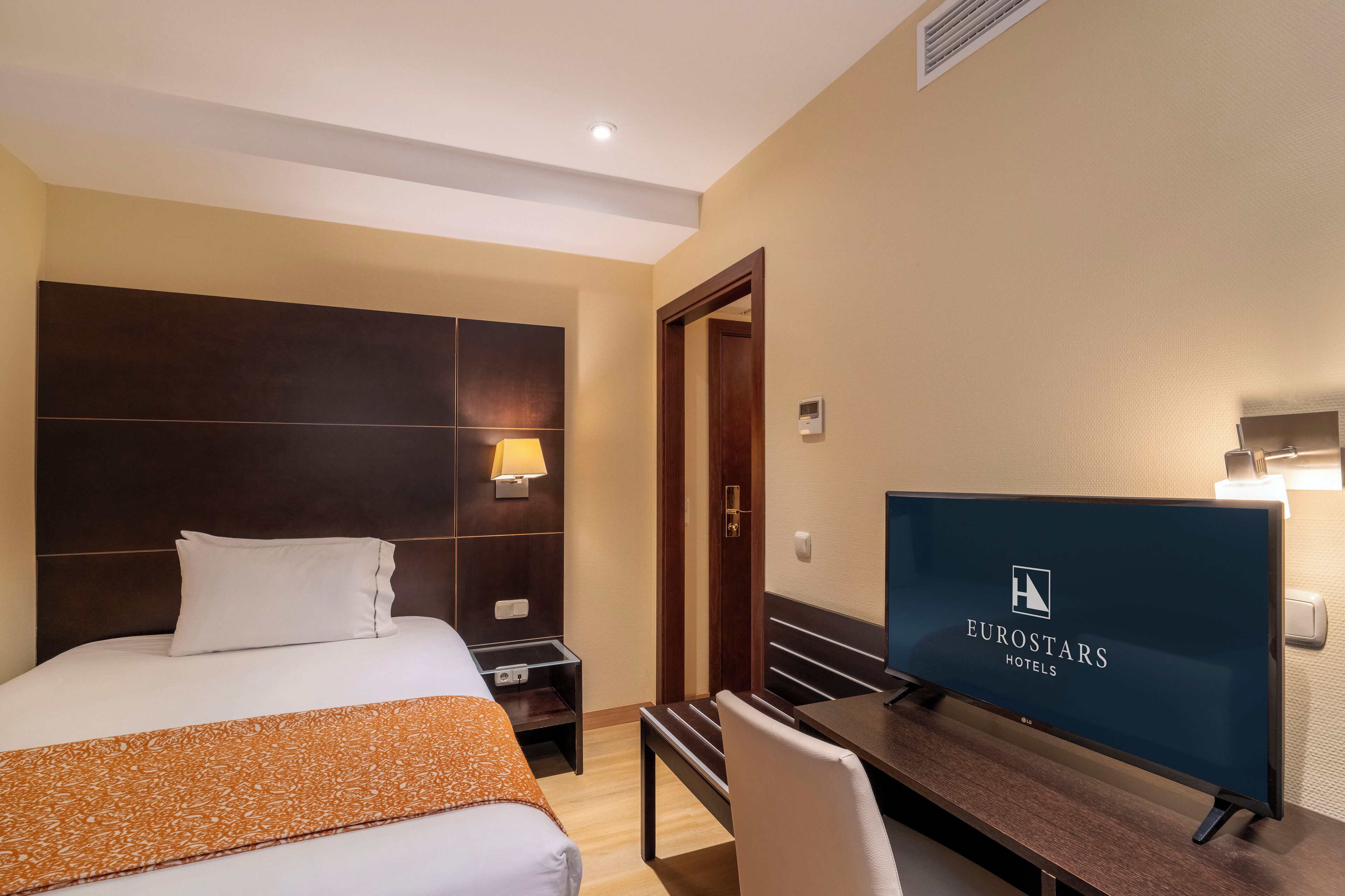 Una habitación de hotel con cama, escritorio, televisor y puerta.