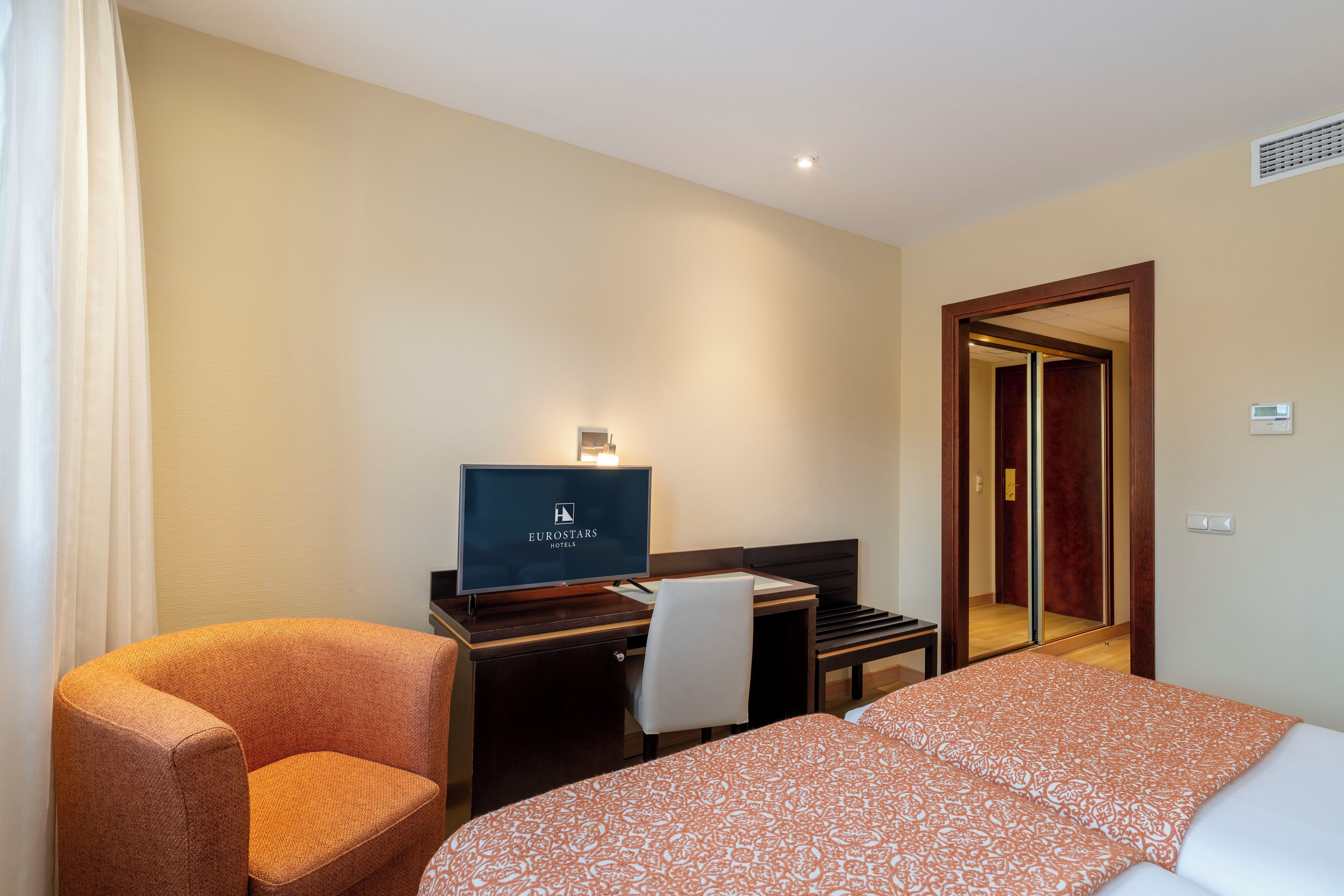 Una habitación de hotel con una cama, un escritorio con computadora, una silla y un televisor.