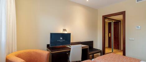 A hotel room with a bed, a desk with a computer, a chair, and a television.
