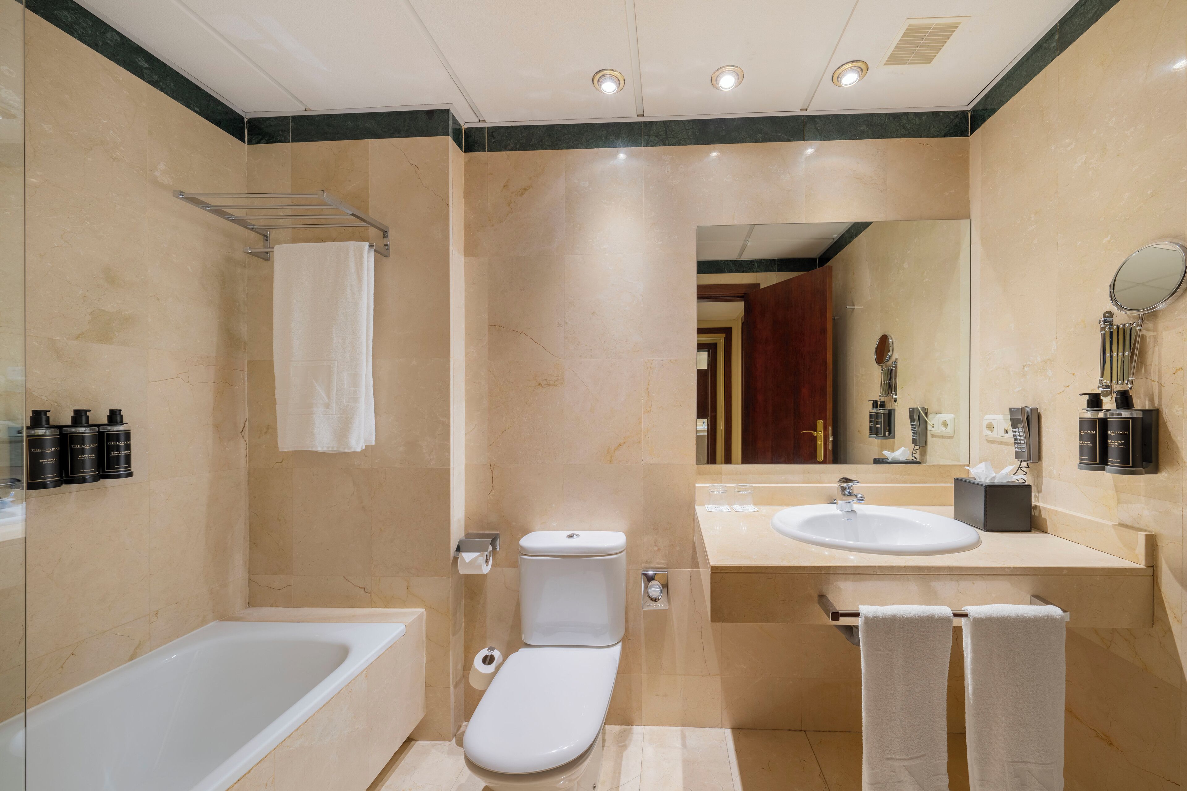 Un baño moderno con bañera, inodoro y lavabo. Hay toallas y artículos de aseo en la encimera.