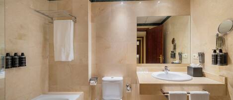 Un baño moderno con bañera, inodoro y lavabo. Hay toallas y artículos de aseo en la encimera.