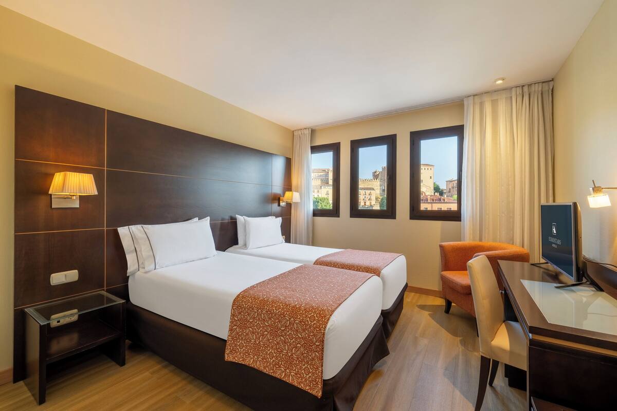 Een hotelkamer met twee bedden, een bureau, een stoel en een televisie.