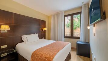 Una habitación de hotel con una cama grande, dos lámparas de noche, un televisor montado en la pared y una ventana con cortinas.
