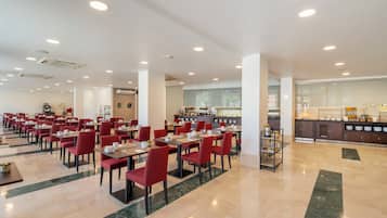 A spacious dining area with red chairs and tables, a kitchen in the background, and a clean, modern design.