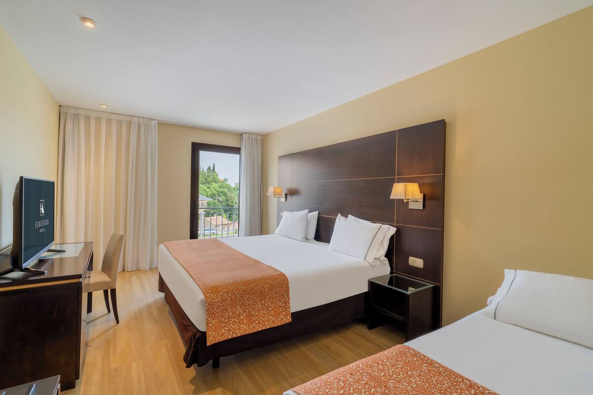 Een hotelkamer met twee bedden, een bureau, een televisie en een raam met gordijnen.