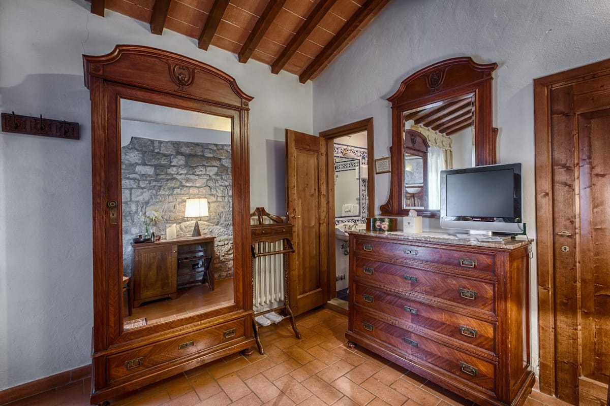 Una habitación con pared de piedra, muebles de madera, un televisor y suelo de baldosas.