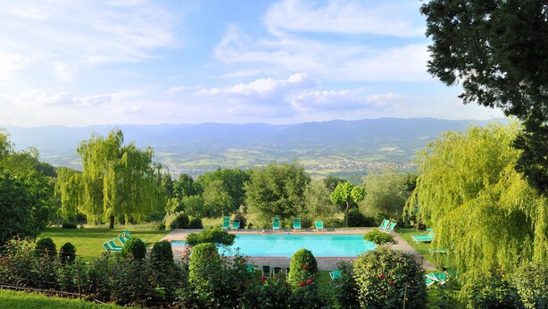 Una piscina con sillas de descanso, rodeada de abundante vegetación y árboles, con vistas a montañas distantes.