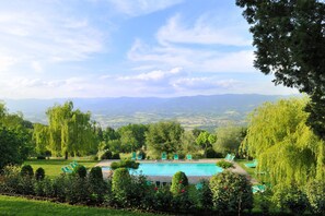 Une piscine bordée de chaises longues, entourée d’une végétation luxuriante et d’arbres, et offrant une vue sur les montagnes lointaines.