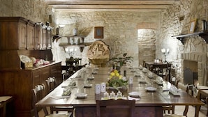 Una larga mesa de comedor lista para una comida en una habitación con paredes de piedra, muebles de madera y un candelabro.