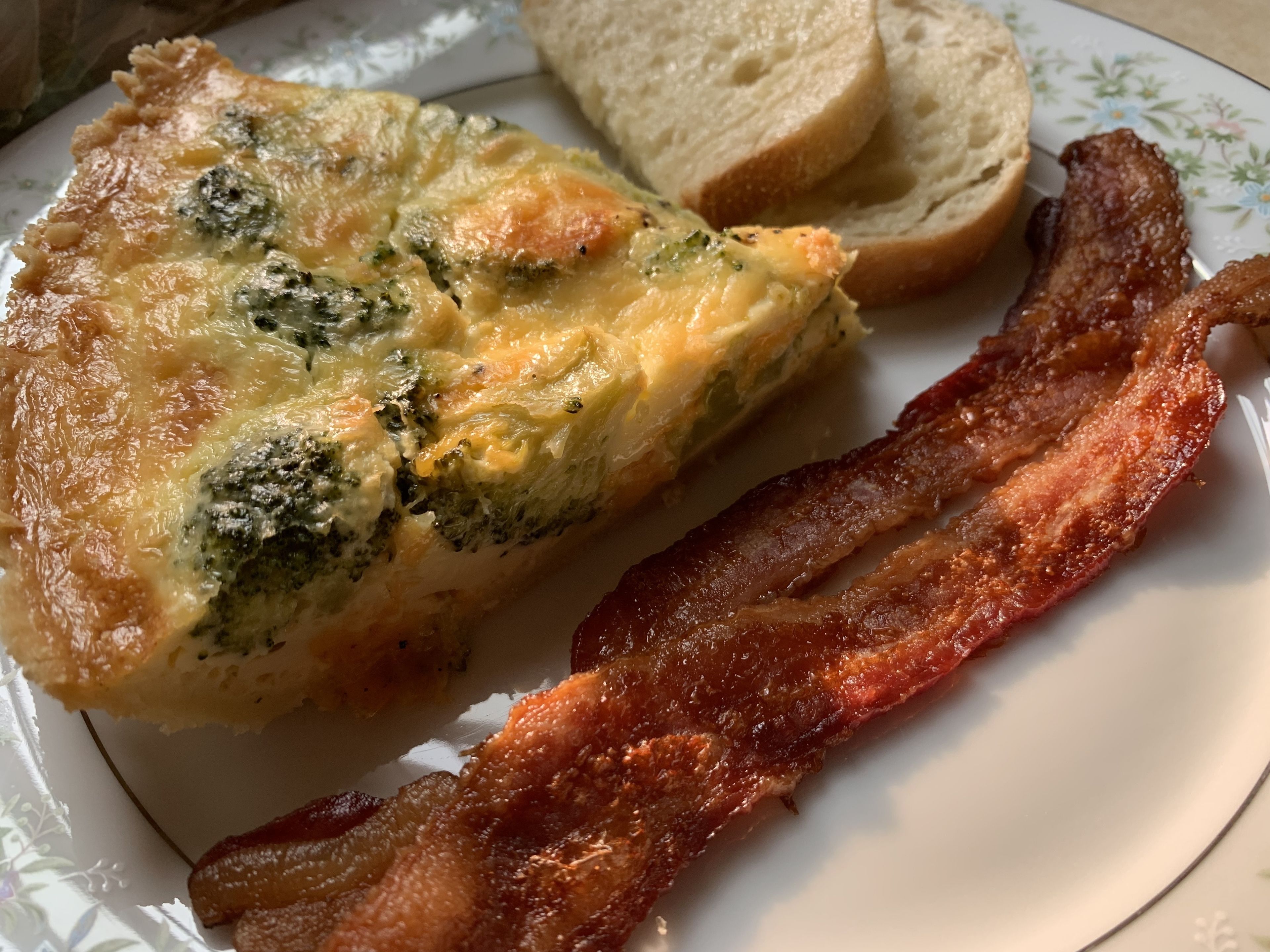 Une assiette avec une part de quiche, deux tranches de pain grillé et une tranche de bacon.