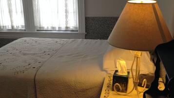A neatly made bed with a floral-patterned bedspread, a bedside lamp with a tissue box, and a patterned rug on the floor.