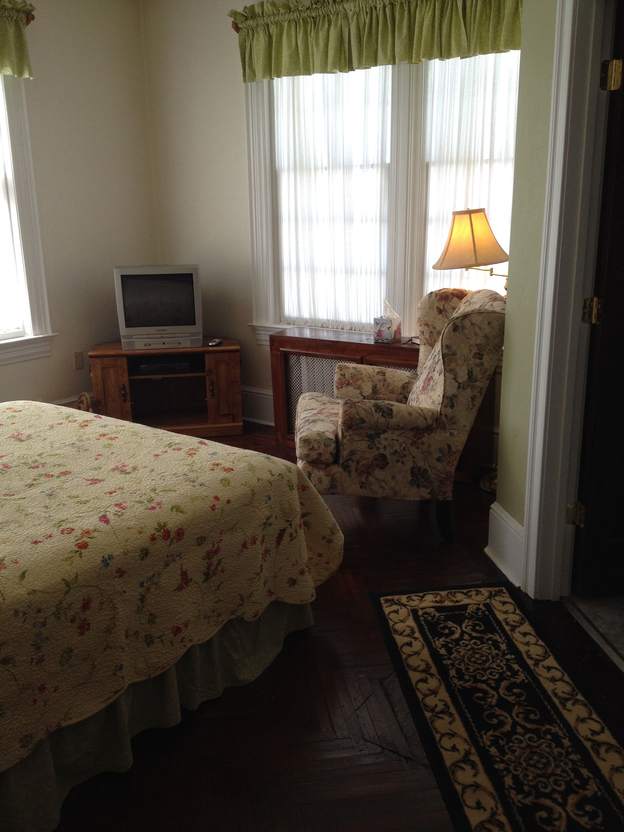 A bedroom with a bed, a chair, a desk, a television, and a lamp.