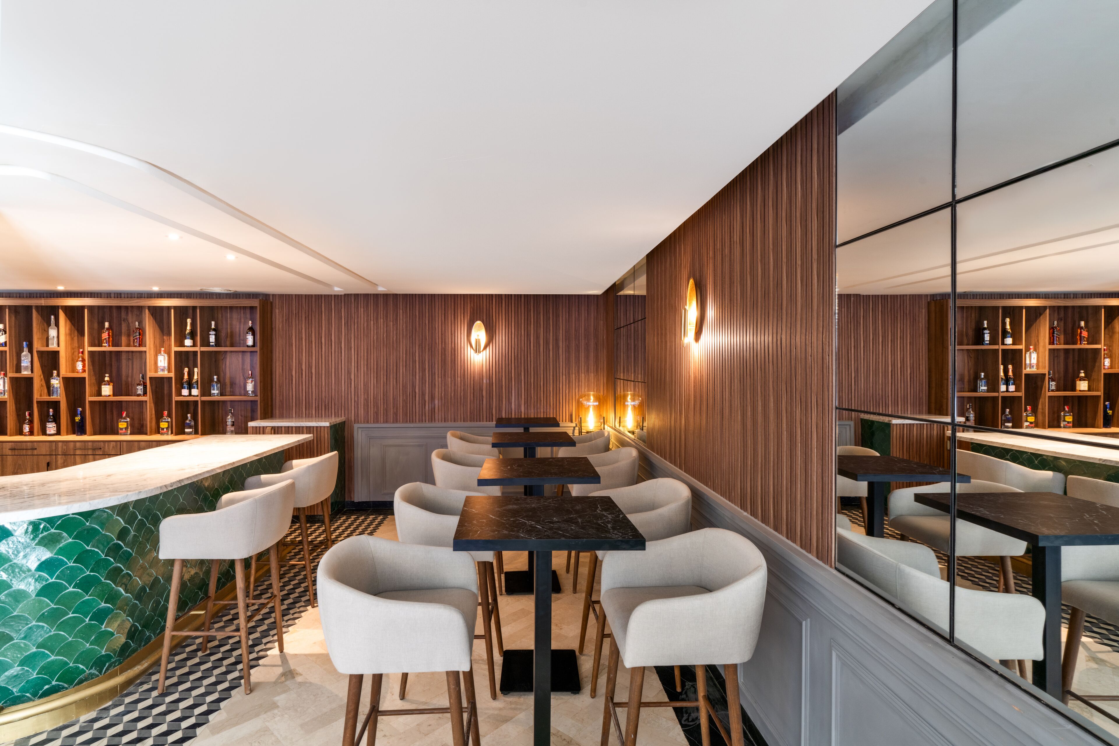 Zona de bar moderna con taburetes altos, una barra larga y estantes llenos de botellas.