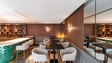 Zona de bar moderna con taburetes altos, una barra larga y estantes llenos de botellas.