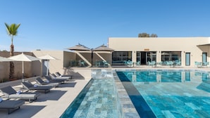 A swimming pool with lounge chairs and umbrellas, a palm tree, and a building with large windows and a flat roof. - Kenzi Rissani Hotel (Errachidia)