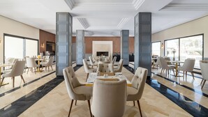 A spacious dining area with a long table and multiple chairs, a fireplace, and large windows providing natural light. - Kenzi Rissani Hotel (Errachidia)