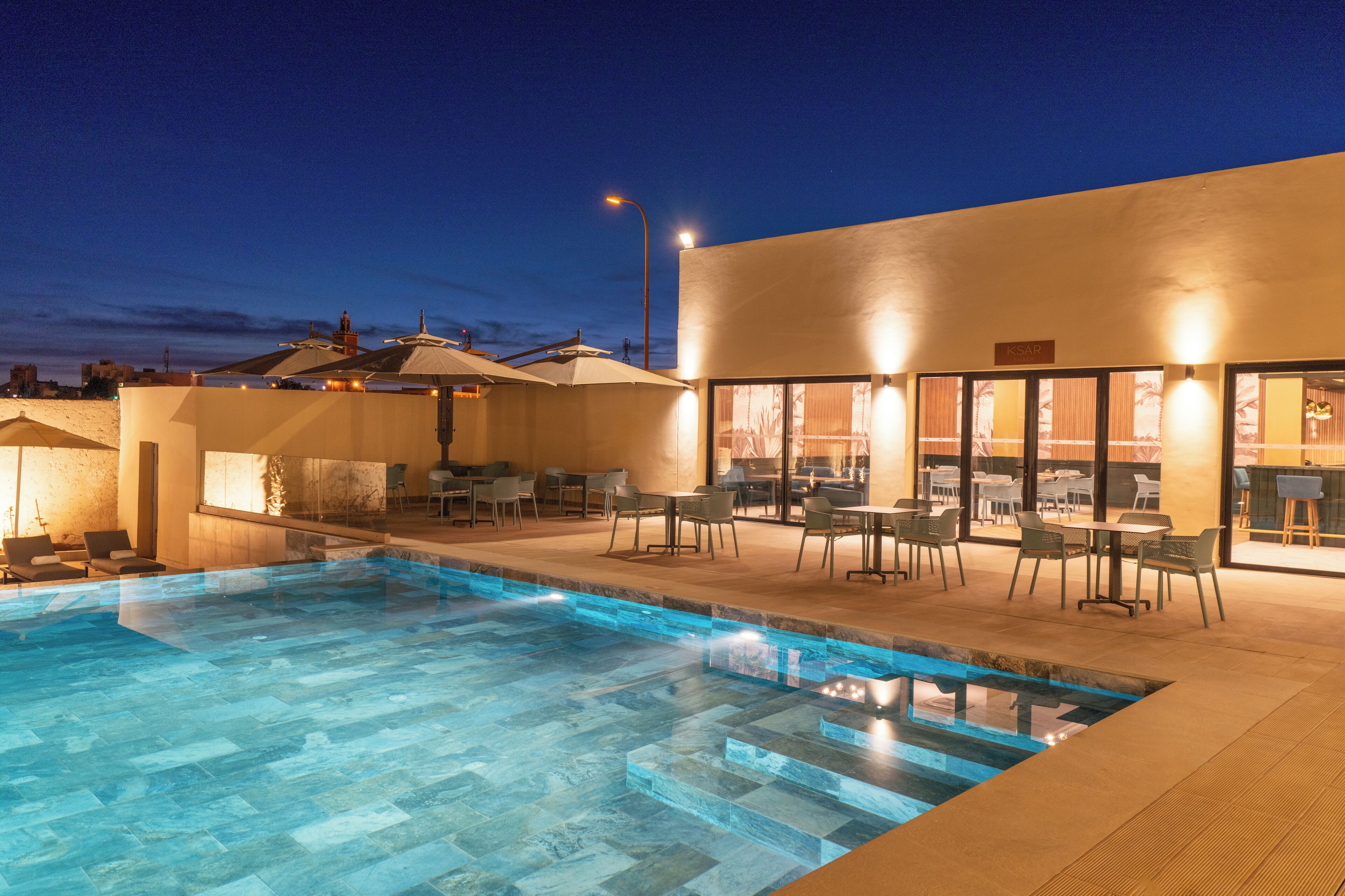 Ein Hotelpoolbereich mit klarem Pool, Liegestühlen und einem Außenbereich zum Essen mit Sonnenschirmen.