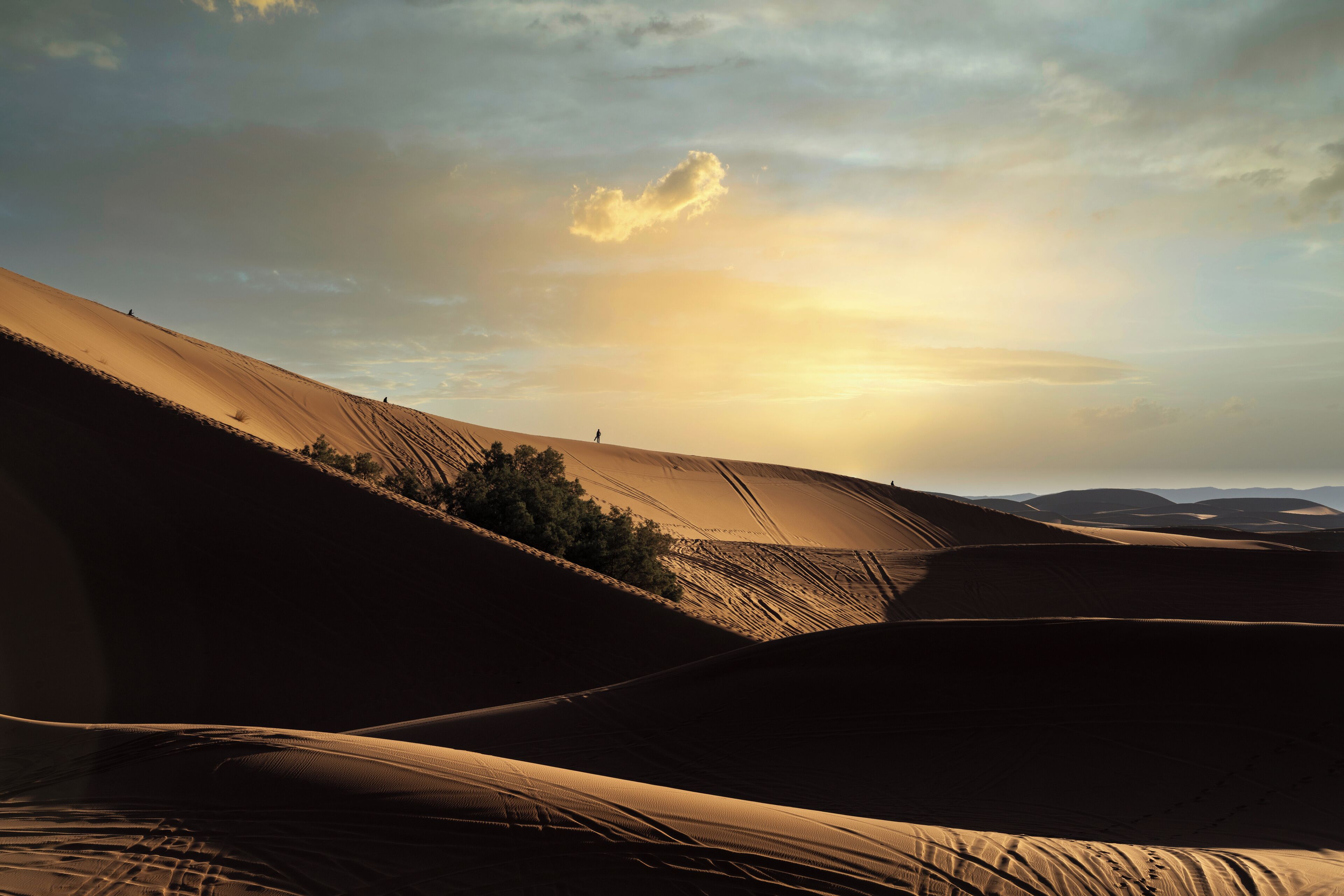 A desert landscape with sand dunes and a person walking.
