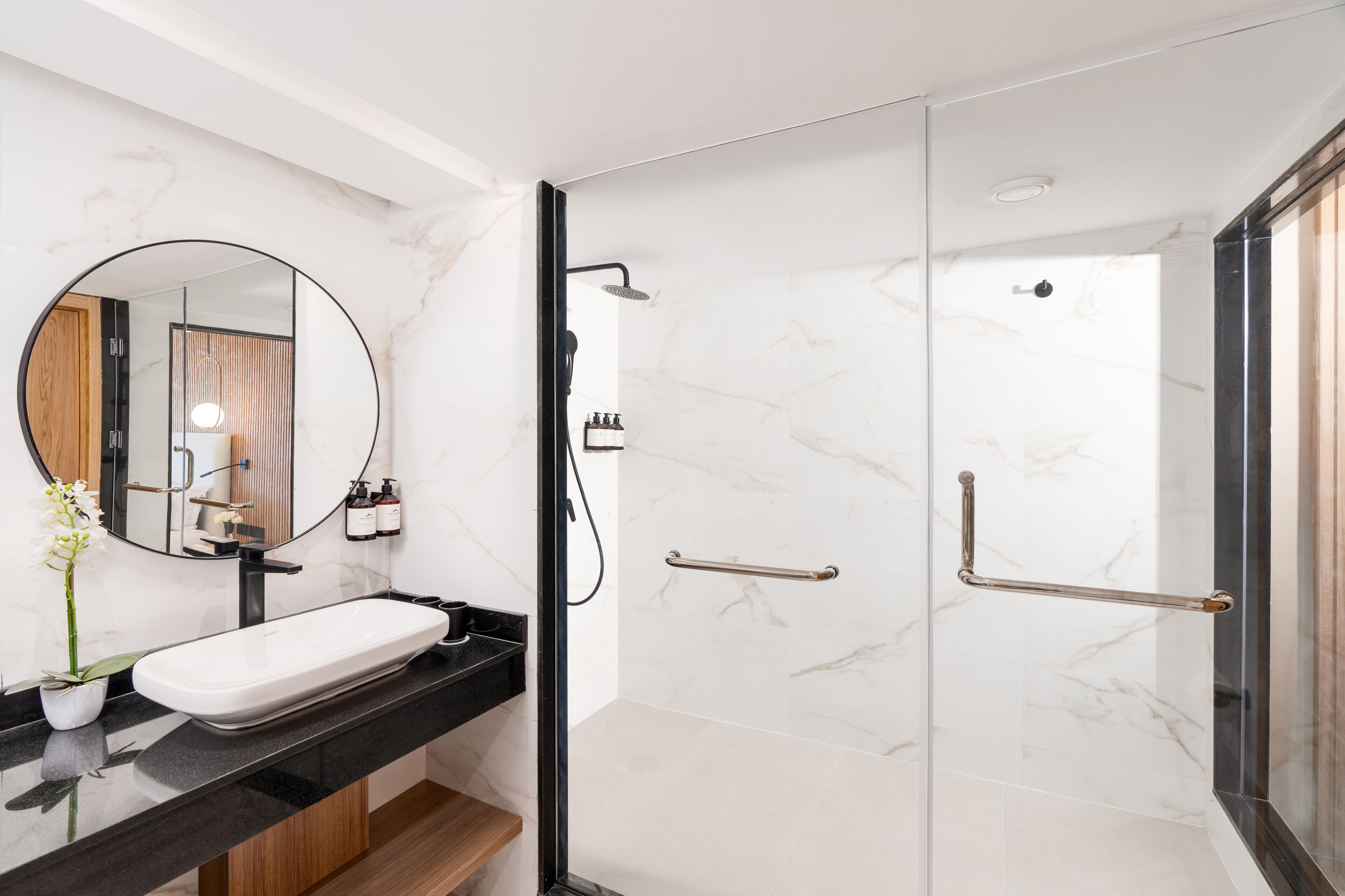 Un baño moderno con lavamanos de mármol, un espejo redondo y zona de ducha con mampara de cristal.