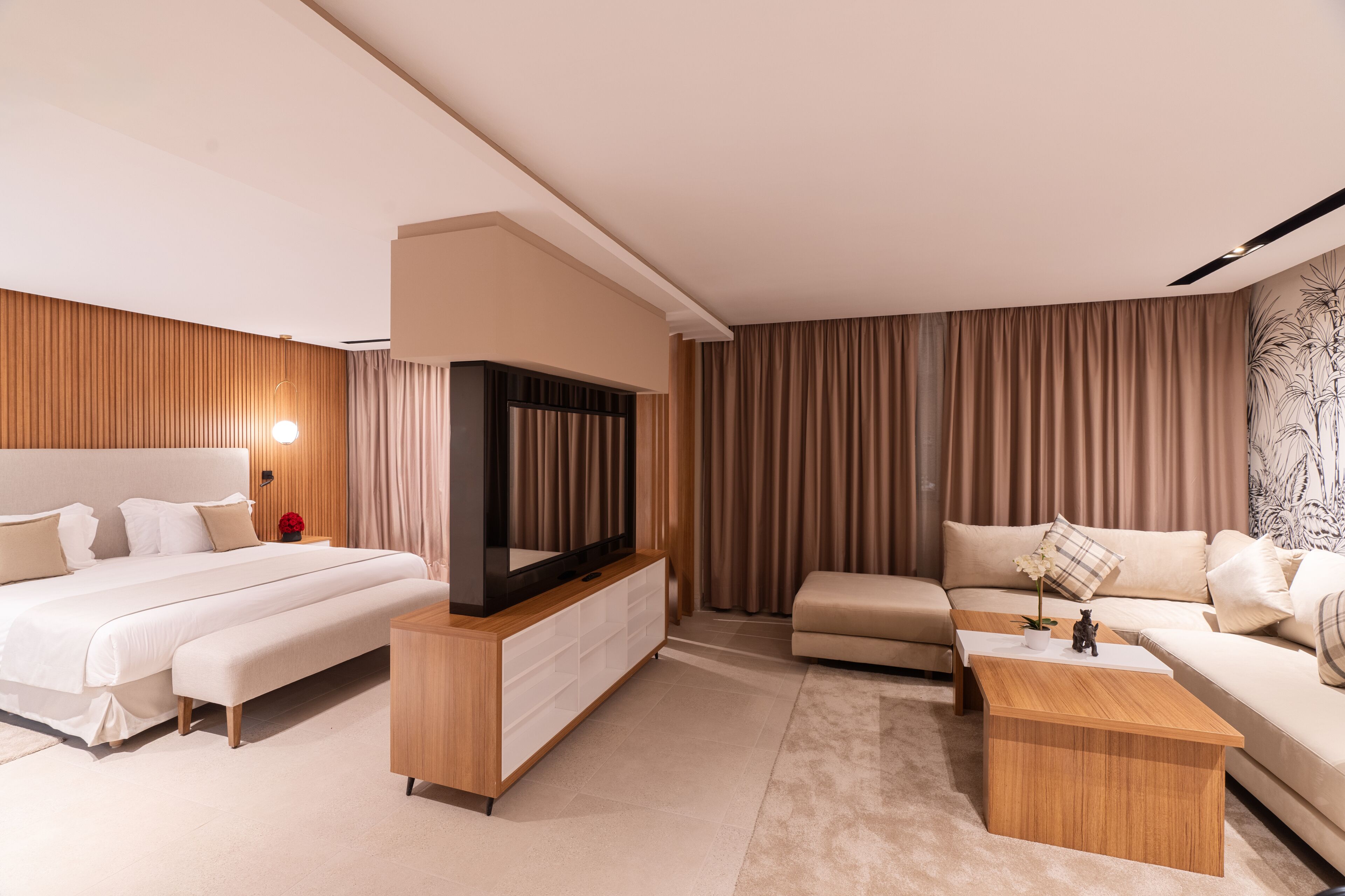 A modern hotel room with a large bed, a sofa, a coffee table, and a TV.