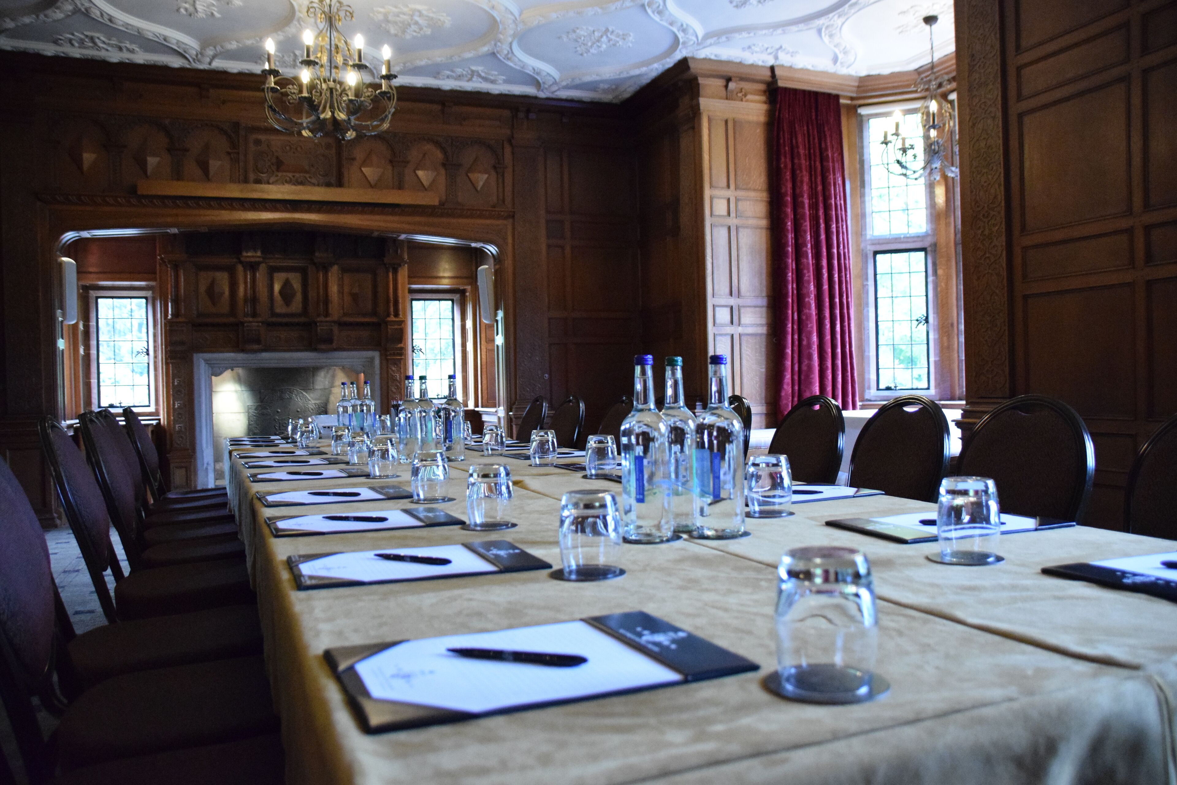 A conference room with a long table set for meetings, wooden paneling, and a fireplace.