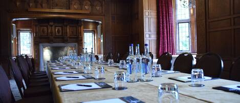 A conference room with a long table set for meetings, wooden paneling, and a fireplace.