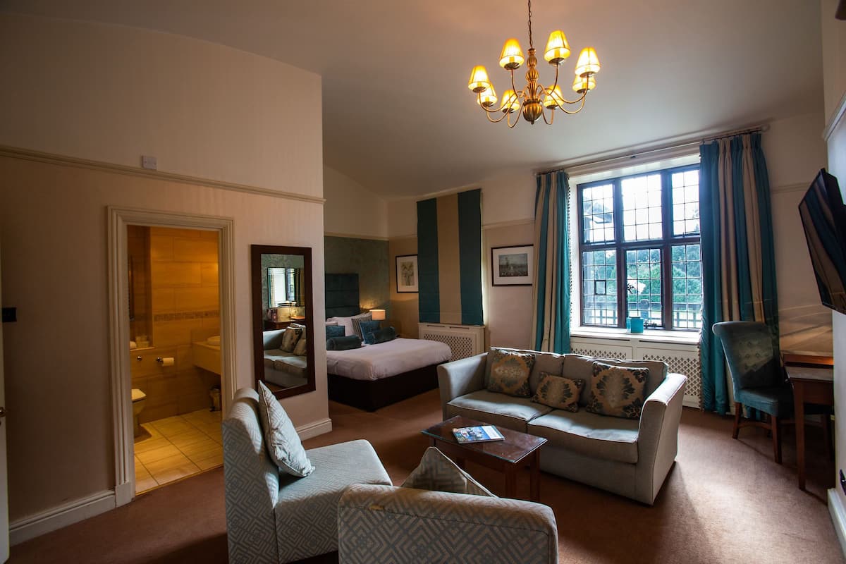 A hotel room with a bed, two sofas, a coffee table, a TV, and a large window with curtains.