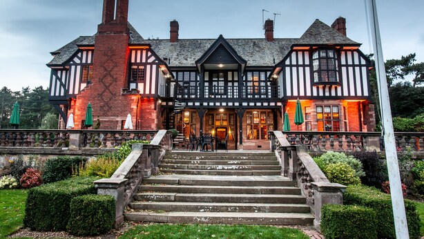 Ein traditionelles Gebäude im Tudor-Stil mit symmetrischer Fassade, einem zentralen Eingang und einer Treppe, die zu den Haupttüren führt.
