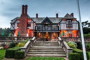A traditional Tudor-style building with a symmetrical facade, a central entrance, and a staircase leading to the main doors. - Inglewood Manor (Ellesmere Port)