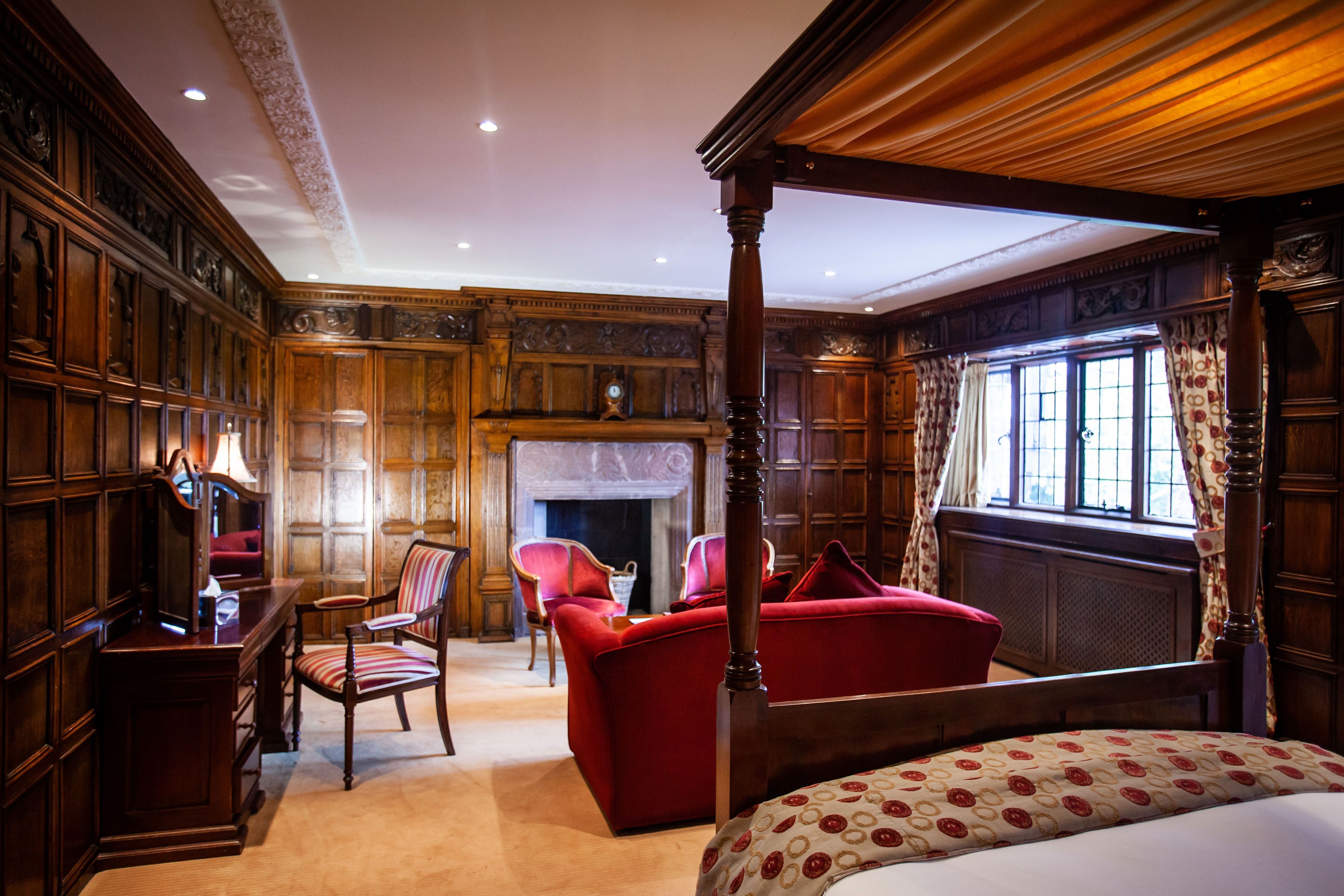 A traditional bedroom with a four-poster bed, a fireplace, and a large window with curtains.