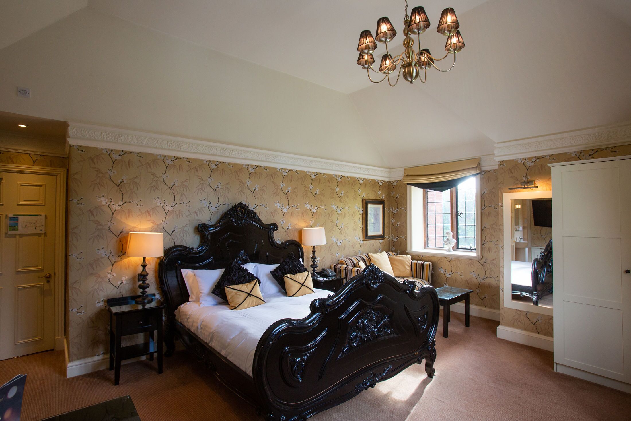 A bedroom with a large bed, two bedside tables, a chandelier, and a window with curtains.