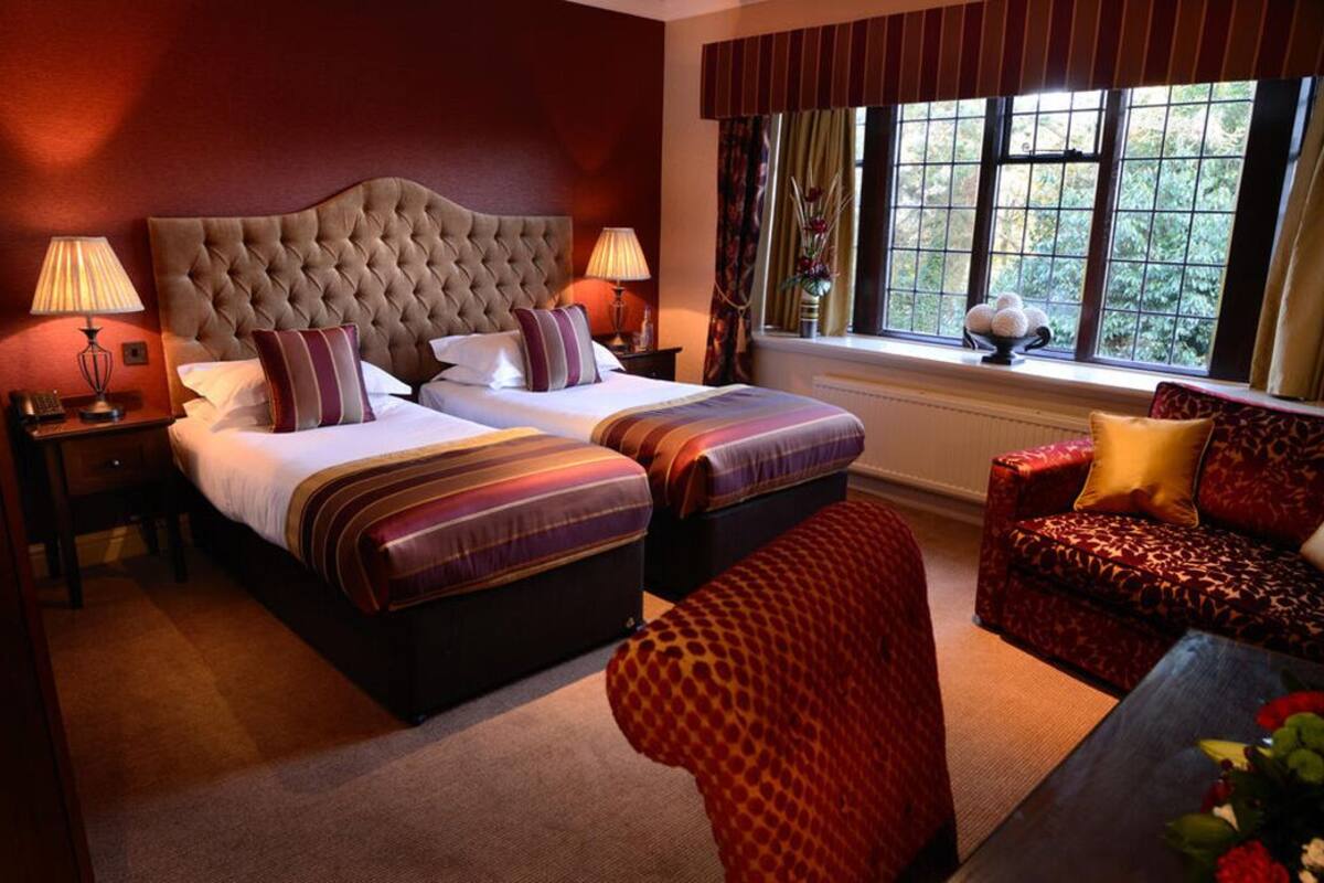A hotel room with a large bed, two bedside tables, a sofa, and a window with curtains.